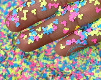 May include: A close-up of a hand holding a variety of colorful Mickey Mouse shaped glitter. The glitter is in shades of pink, yellow, and blue.