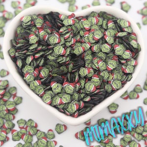 May include: A heart-shaped white bowl filled with green, red, and black polymer clay pieces. The clay pieces are shaped like a green face wearing a red Santa hat. The pieces are scattered around the bowl.