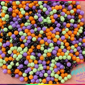 May include: A close-up of a variety of colorful sprinkles, including orange, green, purple, and black. The sprinkles are small and round, and they are perfect for decorating cakes, cupcakes, and other desserts.
