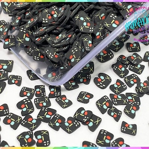 May include: A close-up of a large quantity of black and white game controller shaped resin charms with red and blue accents. The charms are scattered on a white surface.