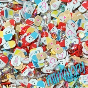 May include: A variety of colorful resin charms in the shape of pills, bandages, and hearts. The charms are scattered on a white surface.