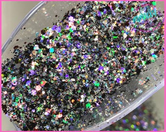 May include: A close-up of a scoop filled with black glitter with iridescent and holographic accents. The glitter is a mix of different sizes and shapes.