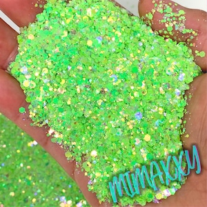 May include: Green and iridescent glitter with a holographic finish. The glitter is loose and has a variety of sizes. The glitter is in a hand and the word "mimakxu" is written in green and white letters on the glitter.