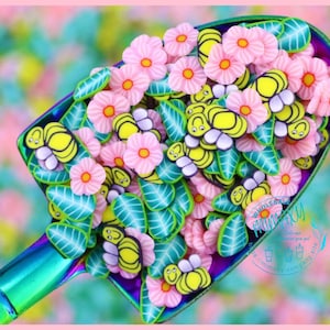 May include: A scoop filled with colorful polymer clay charms. The charms are shaped like flowers, leaves, and bees. The flowers are pink and white, the leaves are green, and the bees are yellow with black eyes. The charms are perfect for adding a touch of whimsy to your crafts.