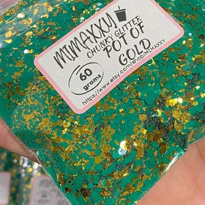 May include: A clear plastic bag filled with chunky green and gold glitter. The label reads "MIMAXXY CHUNKY GLITTER POT OF GOLD" and "60 grams". The glitter is a mix of shapes and sizes.
