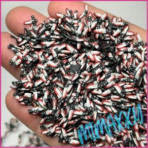 May include: A large pile of black and white knife-shaped resin embellishments with red accents. The embellishments are scattered on a hand.