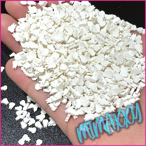 May include: A large pile of white, small, plastic,  decorative charms in the shape of a variety of objects, including hearts, stars, and other abstract shapes. The charms are scattered on a hand.