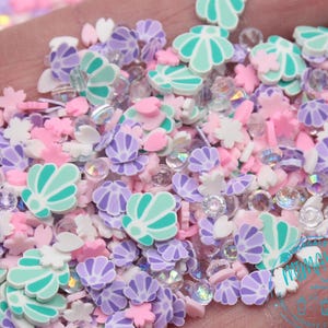 May include: A mix of pastel-colored resin charms, including seashells, flowers, and other shapes. The charms are scattered on a hand, and some are iridescent.