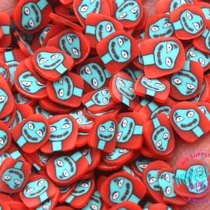 May include: Red and blue resin flatback charms with a cartoon face design. The charms are shaped like a square with rounded corners.