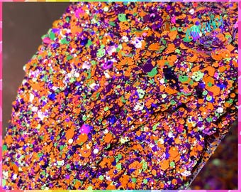Op de afbeelding: Een close-up van een mix van oranje, groene, paarse en witte glitter. De glitter is een mix van verschillende maten en vormen.