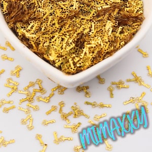 May include: A white ceramic bowl filled with small, gold-colored key-shaped charms. The charms are scattered on a white surface. The image includes the text "MIMAXXXU" in a colorful, iridescent font.