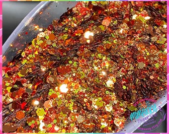 Op de afbeelding: Een close-up van een mengsel van rode, oranje, gouden en groene glitter. De glitter zit in een doorzichtige container en is perfect voor knutselprojecten.