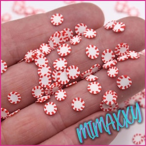 May include: A collection of red and white candy cane sprinkles. The sprinkles are small and round, with a white center and red stripes around the edge.