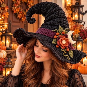 May include: A black crocheted witch hat featuring a curled top, a wide brim, and a dark purple band. The hat is decorated with a cluster of crocheted autumn-colored flowers, green leaves, small orange berries, and a cream-colored crescent moon.
