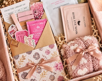 May include: A gift box containing a collagen sheet mask, rose eye mask, a pair of fuzzy pink and white socks tied with a ribbon, a floral patterned book, a library card, stickers, a tea bag, and a gold metal bookmark.