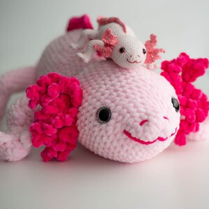 K&ouml;nnte beinhalten: Ein rosa geh&auml;keltes Axolotl-Pl&uuml;schtier mit einem kleineren rosa geh&auml;kelten Axolotl-Pl&uuml;schtier auf dem Kopf.
