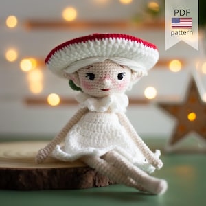 May include: A crochet doll featuring a wide, red and white mushroom-shaped hat, white hair, and a white dress with a ruffled collar. The doll has a light beige complexion with pink cheeks, dark eyes, and a small red mouth, presented as a PDF pattern.
