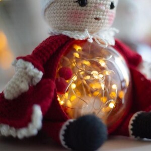 Peut inclure: Poup&eacute;e du P&egrave;re No&euml;l au crochet avec un corps en globe de verre transparent rempli de guirlandes lumineuses blanc chaud. La poup&eacute;e porte un manteau rouge avec des bordures blanches, un chapeau blanc et des bottes noires.