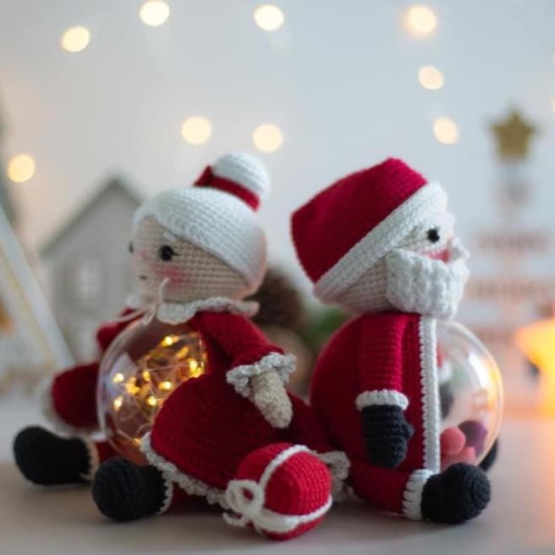 Peut inclure: Deux ornements de No&euml;l crochet&eacute;s repr&eacute;sentant le P&egrave;re No&euml;l et la M&egrave;re No&euml;l. Les figurines sont rouges et blanches, avec des chaussures et des gants noirs. Chaque figurine est &agrave; l'int&eacute;rieur d'une boule de verre transparente, avec des lumi&egrave;res &agrave; l'int&eacute;rieur de l'ornement de la M&egrave;re No&euml;l.