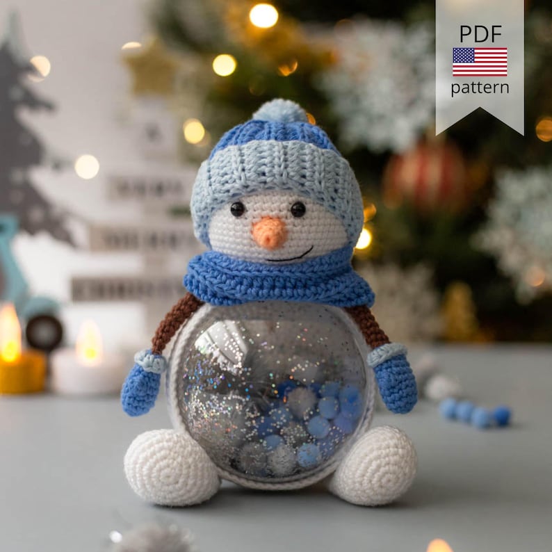 May include: A crocheted snowman with a blue hat, scarf, and mittens. The snowman has a carrot nose and a smiling face. The clear glass body is filled with silver and blue decorative elements. The image includes a banner that says "PDF pattern".