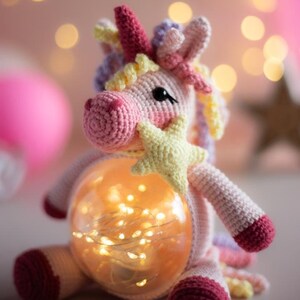 May include: A crocheted unicorn lamp in shades of pink, white, and purple. The unicorn has a pink horn, black eyes, and a yellow star. The lamp features a glowing orb filled with warm white fairy lights.