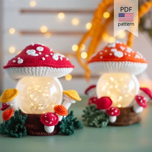 Può includere: Due lampade a forma di fungo all'uncinetto con cappelli rossi e arancioni a pois bianchi, su basi marroni con piccoli funghi colorati e fogliame verde. Ogni lampada contiene una sfera di vetro con luci a LED bianco caldo. PDF pattern.