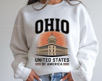 Könnte beinhalten: Weißes Sweatshirt mit einer Grafik des Ohio Statehouse, dem Wort "OHIO" darüber und "UNITED STATES OF AMERICA" darunter. Das Design beinhaltet einen orangefarbenen Sonnenuntergangshintergrund.