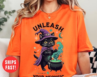 May include: Orange t-shirt featuring a cartoon black cat wearing a witch hat and cape, with the text "UNLEASH YOUR MEOWGIC". The cat is next to a bubbling cauldron. The shirt is a Halloween-themed design.