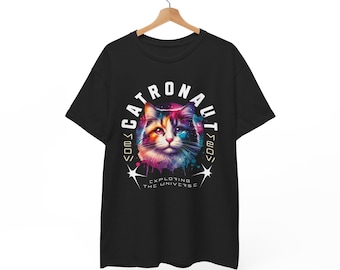 May include: Black t-shirt featuring a colourful cat astronaut design. The cat is wearing a space suit and has a galaxy background. The text reads "Catronaut" and "Exploring the Universe".