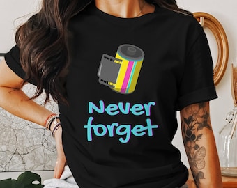 May include: Black t-shirt featuring a colorful film roll graphic with yellow, pink, and teal stripes. The words "Never forget" are written in a teal and blue gradient font below the graphic. A casual, everyday tee.