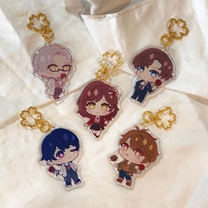 Puede incluir: Cinco llaveros acrílicos con personajes de anime estilo chibi. Cada llavero tiene un cierre dorado en forma de flor. Los personajes están en diferentes atuendos y poses, cada uno sosteniendo una rosa.