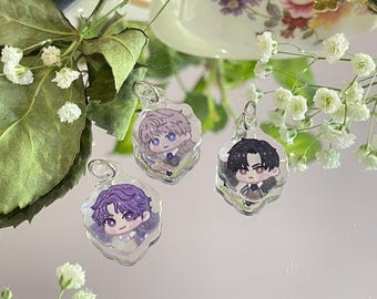 May include: Three clear acrylic charms featuring anime-style character illustrations. Each charm has a silver-colored metal loop at the top. The characters have different hair colors: purple, light purple, and black. The background is a reflective surface with floral accents.