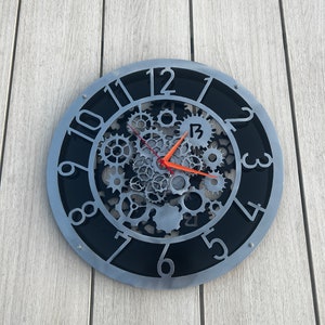May include: A silver and black clock with a gear design. The clock face has Roman numerals and the hands are red and silver.