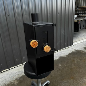 Puede incluir: Una estufa de leña de metal negro con una pequeña puerta y dos pomos de madera. La estufa está sentada en una silla de oficina negra con ruedas.