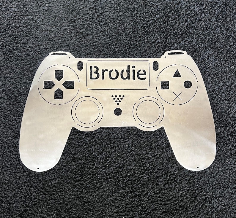 May include: A silver metal cutout of a video game controller with the name "Brodie" in the center.