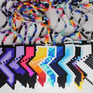 May include: A collection of colorful beaded necklaces with pixelated pendants in various colors, including purple, pink, yellow, and blue. Some necklaces have the word "EXCISION" spelled out in beads.