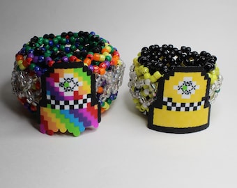 Peut inclure: Deux bracelets en perles avec des breloques de taxi pixelisées. Le bracelet de gauche a des perles arc-en-ciel et un charme de taxi arc-en-ciel. Le bracelet de droite a des perles noires, jaunes et blanches et un charme de taxi jaune.
