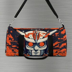 May include: A black duffel bag with a colourful graphic print of a robot face. The robot has orange eyes and a white and blue helmet. The bag has black straps and a black zipper.