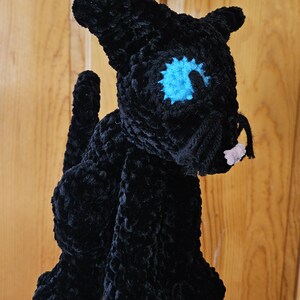 May include: Black crocheted cat plush toy with a blue eye and pink nose.