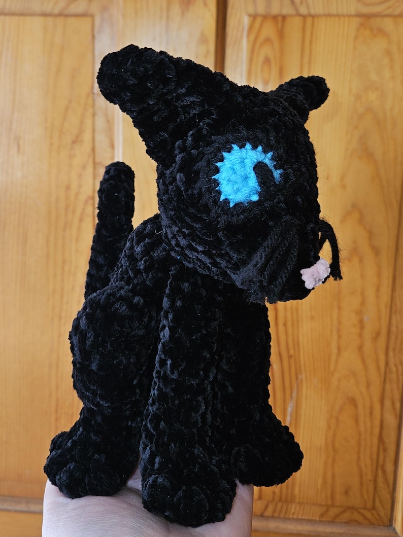 May include: Black crocheted cat plush toy with a blue eye and pink nose.