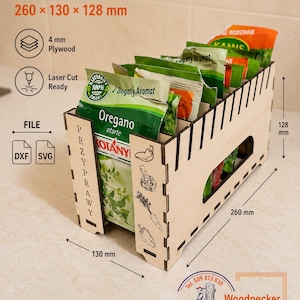 Może przedstawiać: Organizer na przyprawy ze sklejki o wymiarach 260 x 130 x 128 mm. Pudełko posiada wycinane laserowo ilustracje warzyw na boku, pionowo nadrukowane słowo PRZYPRAWY oraz wewnętrzne przegródki mieszczące kilka opakowań z przyprawami.