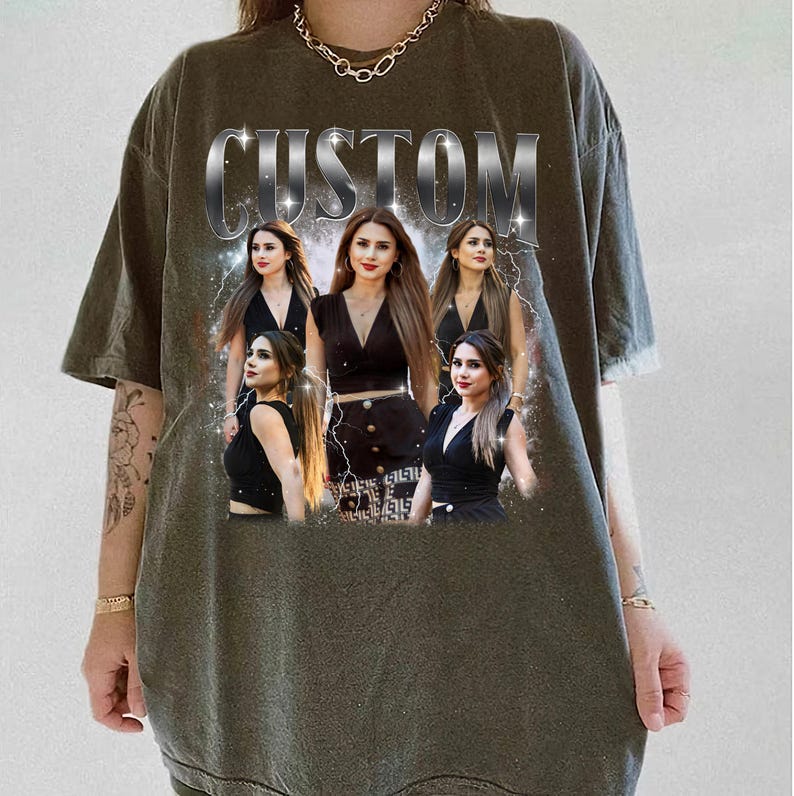 May include: Olive green t-shirt with a custom design featuring a woman in various poses, with the word "CUSTOM" in silver block letters across the top. The woman is wearing a black outfit. The design includes lightning bolt graphics.