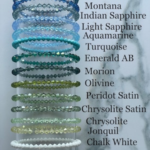May include: A set of 12 crystal bracelets in various colors, including blue, green, and white. Each bracelet is labeled with a different gemstone name, such as Montana AB, Indian Sapphire, and Crystal AB.