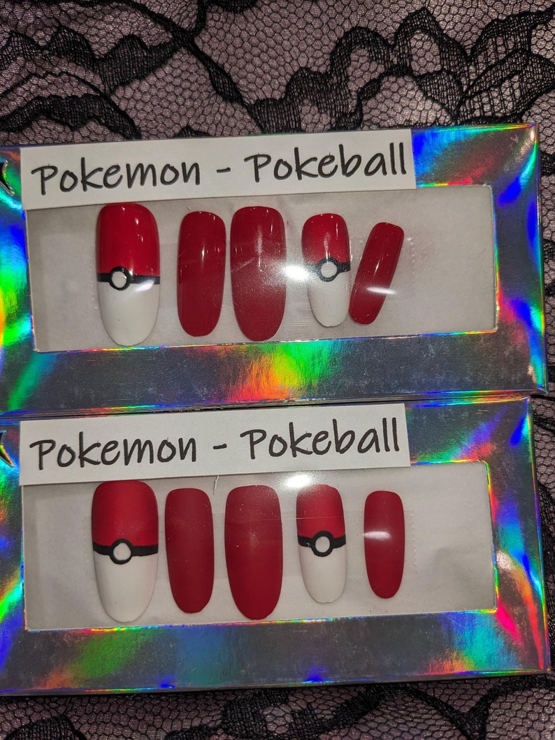 May include: Two sets of fake nails in a clear plastic box. Each set has five nails with a red base and a white tip. One set has a black and white Pokeball design on the thumb nail. The box has the text "Pokemon - Pokeball" on the top.