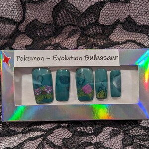 May include: A set of fake nails with a Pokemon theme. The nails are teal green with images of Bulbasaur, Ivysaur, and Venusaur. The box says "Pokemon - Evolution Bulbasaur".