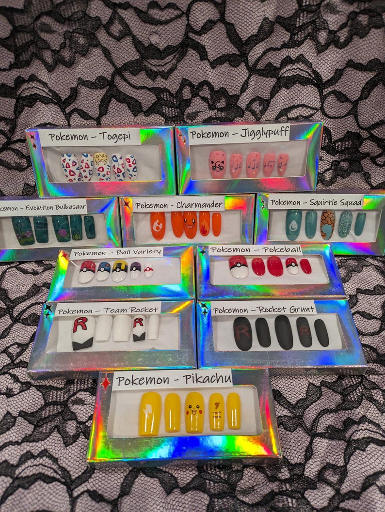 May include: A collection of 10 small boxes, each containing a set of fake nails with a Pokemon theme. The boxes are arranged in two rows of five. The themes include Togepi, Jigglypuff, Evolution Bulbasaur, Charmander, Squirtle Squad, Ball Variety, Pokeball, Team Rocket, Rocket Grunt, and Pikachu.