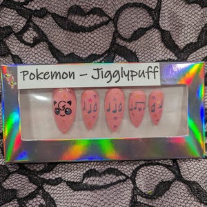 May include: A set of pink press-on nails with a Pokemon Jigglypuff design. The nails feature a cartoon Jigglypuff with stars and musical notes.