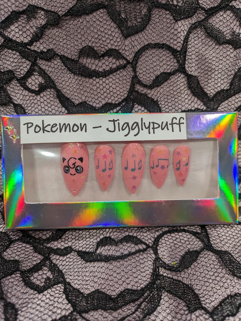 May include: A set of pink press-on nails with a Pokemon Jigglypuff design. The nails feature a cartoon Jigglypuff with stars and musical notes.