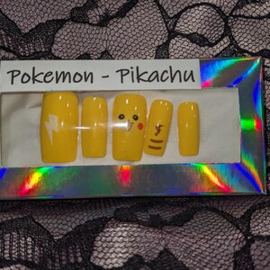 May include: A set of yellow press-on nails with a Pikachu theme. The nails feature a lightning bolt, Pikachu's face, and a tail.