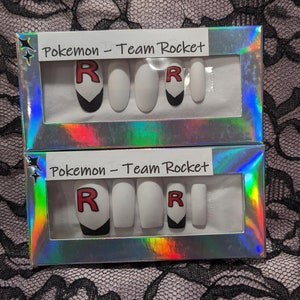 May include: Two sets of fake nails in a clear plastic box with a holographic finish. Each set has five nails with a white base and a black and red "R" design. The box has the text "Pokemon - Team Rocket" printed on it.
